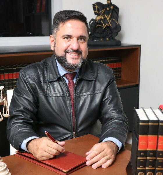 Dr Marcelo Galvão em seu escrit[orio sentado na mesa e sorrindo