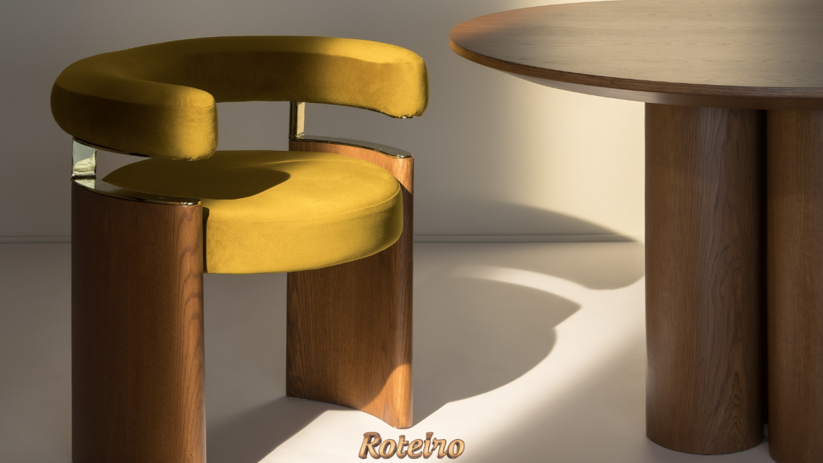 Cadeira Curva BONNI em veludo amarelo mostarda com base em madeira de carvalho e detalhes em latão dourado, ao lado de mesa redonda em madeira — design de Erik Bonissato
