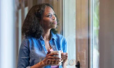 mulher com uma xicara na mão olhando pela janela e pensativa