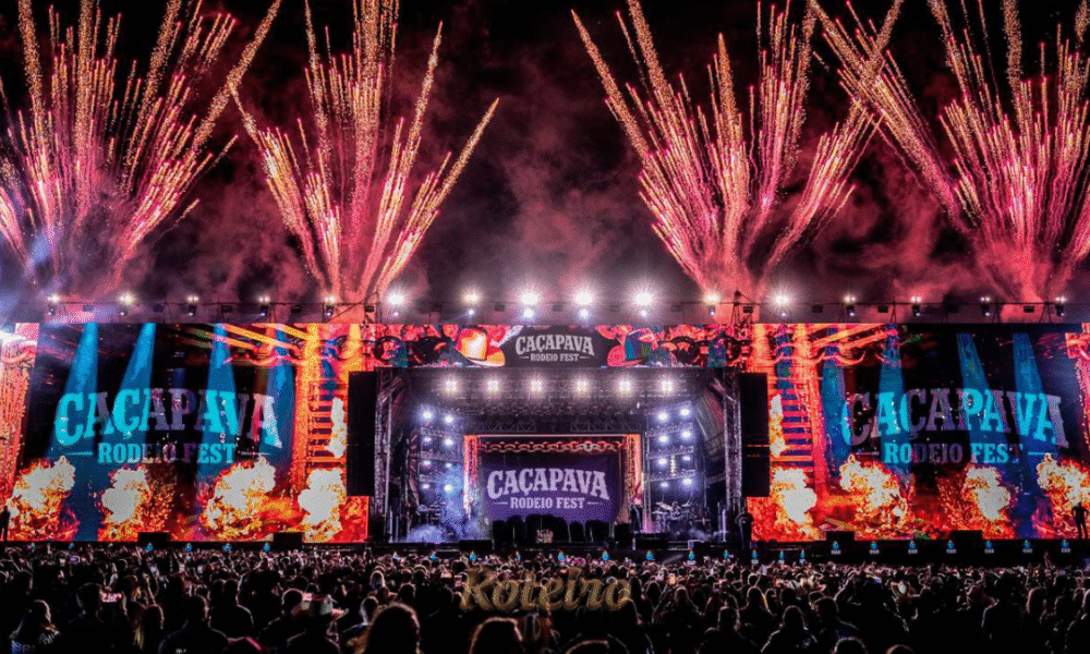 Estrutura gigante da arena e palco do Caçapava Rodeio Fest 2026, capturada à noite com iluminação cênica. A foto destaca a capacidade de público para os shows de Simone Mendes, Alok e Zé Neto & Cristiano, reforçando a importância do evento para o turismo e entretenimento regional no RoteiroSJC