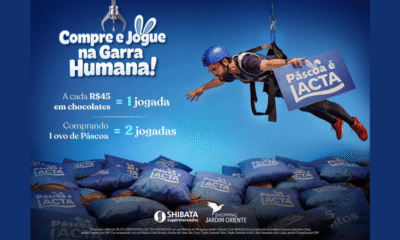 Pessoa suspensa por cabos de segurança sobre uma máquina gigante repleta de almofadas e brindes de chocolate no Shopping Jardim Oriente, promoção Garra Humana de Páscoa sjc