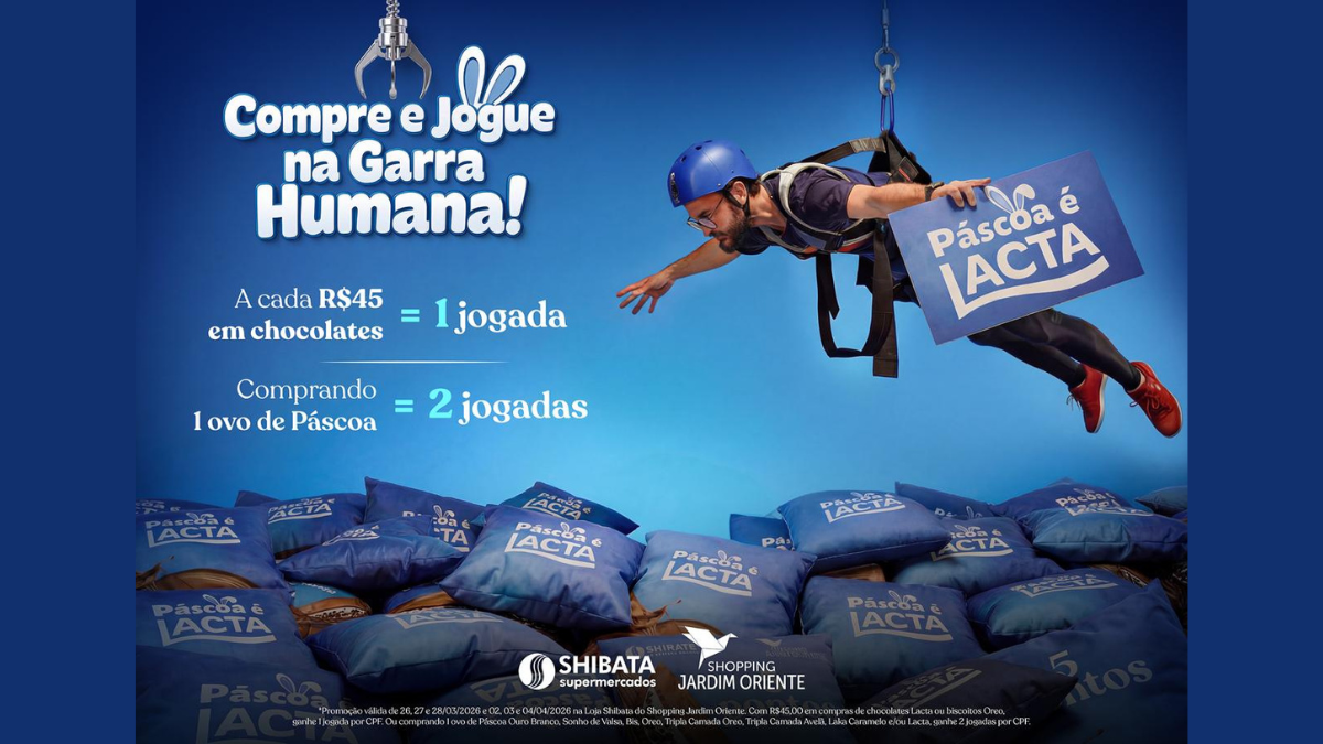Pessoa suspensa por cabos de segurança sobre uma máquina gigante repleta de almofadas e brindes de chocolate no Shopping Jardim Oriente, promoção Garra Humana de Páscoa sjc