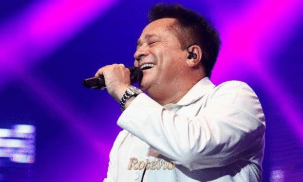 Fotografia de entretenimento mostrando o cantor sertanejo Leonardo no palco da Arena Farma Conde, em São José dos Campos. O artista aparece sorridente, segurando o microfone em um momento de interação com o público. Ao fundo, a estrutura de iluminação do show e a plateia lotada com milhares de fãs na arena, criando uma atmosfera de grande evento e celebração da música sertaneja no Vale do Paraíba