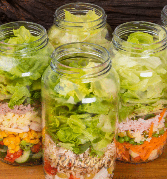 Vários potes de vidro alinhados com saladas coloridas em camadas, prontos para consumo. Exemplo de marmita saudável e econômica preparada para a semana.