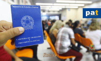 Mão em primeiro plano segurando uma Carteira de Trabalho azul, com fundo desfocado mostrando pessoas em fila para atendimento no PAT de São José dos Campos. No canto superior direito, estão aplicados os logotipos do PAT e, logo abaixo, da Prefeitura Municipal. Vagas de emprego PAT SJC