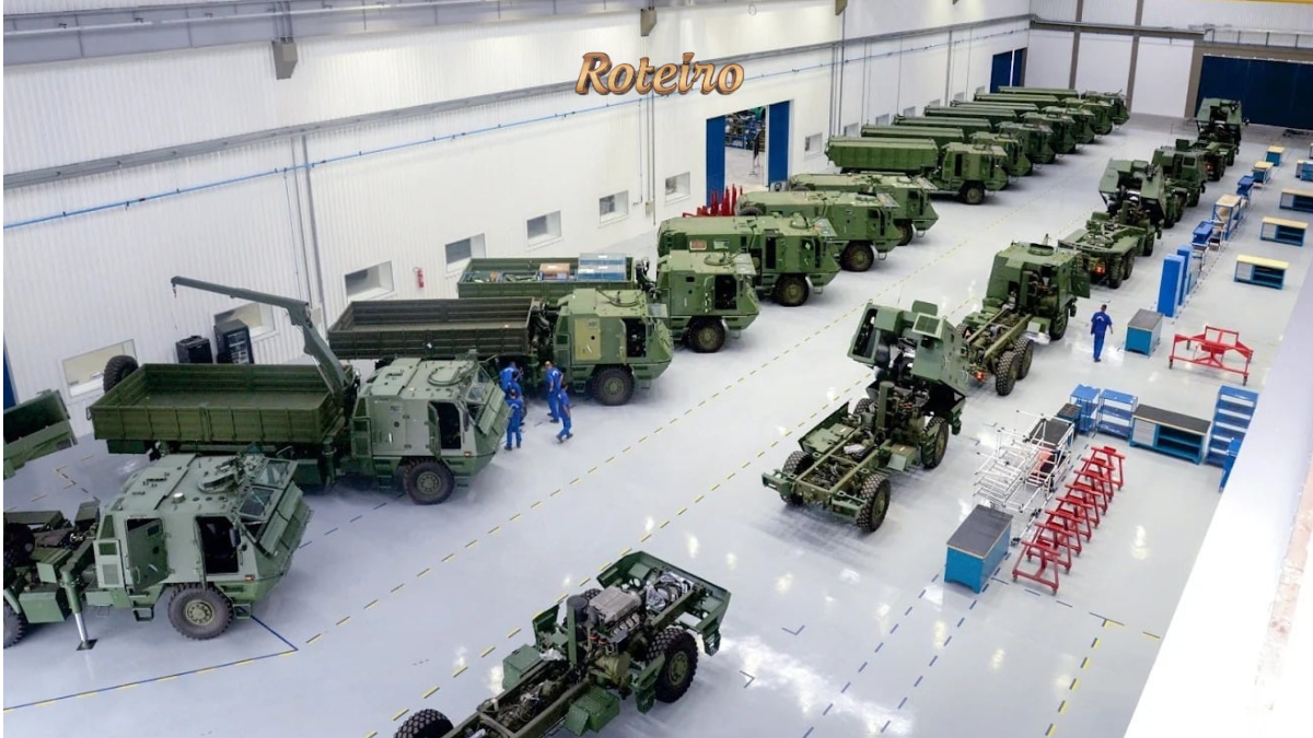 Vista interna de galpão industrial com veículos militares blindados e caminhões de combate na cor verde militar enfileirados, com funcionários com uniformes azuis trabalhando na linha de montagem. Foto: Divulgação/Avibras Aeroco