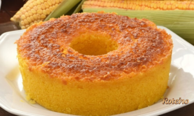 Bolo de milho cremoso assado em forma com furo, dourado e fofinho, com espigas de milho ao fundo — receita junina SJC foto Roteiro SJC