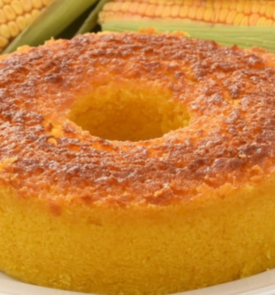 Bolo de milho cremoso assado em forma com furo, dourado e fofinho, com espigas de milho ao fundo — receita junina SJC foto Roteiro SJC
