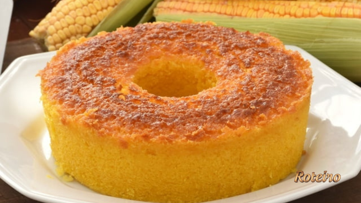 Bolo de milho cremoso assado em forma com furo, dourado e fofinho, com espigas de milho ao fundo — receita junina SJC foto Roteiro SJC