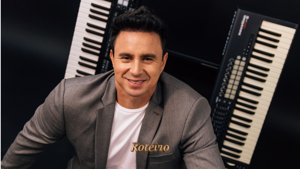 Allen Lima, músico integrante da Família Lima, sorridente em frente a dois teclados musicais, vestindo blazer cinza e camiseta branca em foto de divulgação do espetáculo Brasil em Teclas