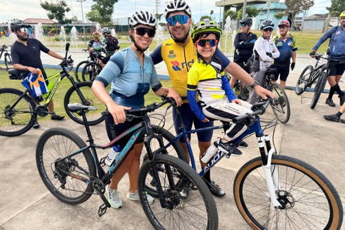 Família composta por casal e criança com capacete e óculos de sol posam sorrindo ao lado de suas bicicletas durante o evento de lançamento do Cicloturismo SJC no Parque Ribeirão Vermelho, em São José dos Campos. Foto: Claudio Vieira/PMSJC