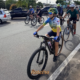 Grupo de ciclistas pedala em ciclovia de São José dos Campos durante o lançamento do programa Cicloturismo SJC, com destaque para ciclista jovem com capacete colorido e uniforme azul e amarelo na frente do pelotão. Foto: Claudio Vieira/PMSJC