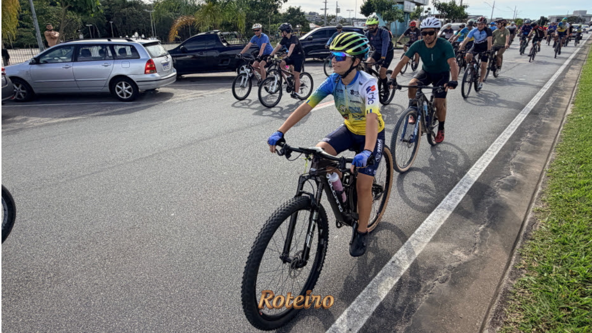 Grupo de ciclistas pedala em ciclovia de São José dos Campos durante o lançamento do programa Cicloturismo SJC, com destaque para ciclista jovem com capacete colorido e uniforme azul e amarelo na frente do pelotão. Foto: Claudio Vieira/PMSJC