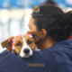 Tutora de costas abraça cachorro pequeno de pelagem caramelo e branca com laço vermelho na cabeça durante evento de castração gratuita do programa Meu Pet Feliz em São José dos Campos. Foto: Divulgação/PMSJC