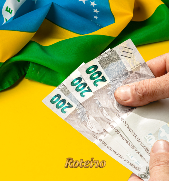 Pessoa segurando nota de dinheiro ao lado de decoração verde e amarela da Copa do Mundo 2026 — foto ilustrativa