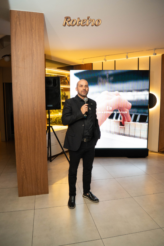 Felipe proprietário da Dalmóbile discursa durante apresentação oficial da coleção 2026, com telão ao fundo exibindo o conceito "Elo" da marca
