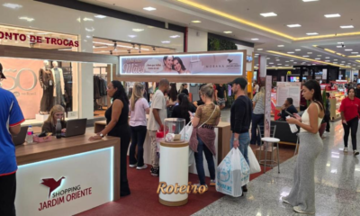 Clientes fazem fila no balcão "Ponto de Trocas" da campanha Dia das Mães do Shopping Jardim Oriente em São José dos Campos, com painel da Morana e movimento intenso no corredor do shopping ao fundo