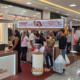 Clientes fazem fila no balcão "Ponto de Trocas" da campanha Dia das Mães do Shopping Jardim Oriente em São José dos Campos, com painel da Morana e movimento intenso no corredor do shopping ao fundo