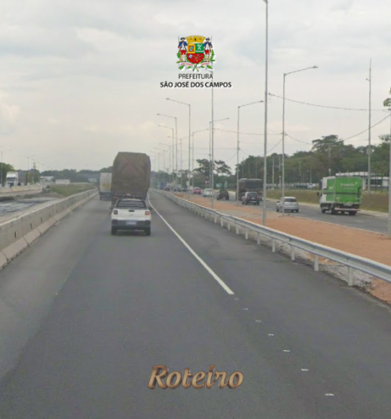 Pista da Rodovia Presidente Dutra em São José dos Campos com veículos em movimento, incluindo caminhão e carro de passeio, ladeada por postes de iluminação e área de obras na marginal esquerda