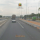 Pista da Rodovia Presidente Dutra em São José dos Campos com veículos em movimento, incluindo caminhão e carro de passeio, ladeada por postes de iluminação e área de obras na marginal esquerda