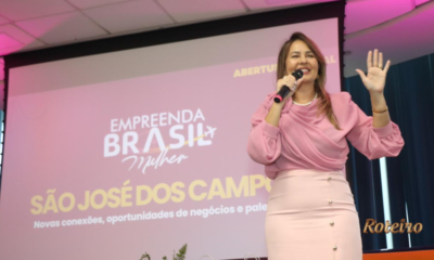 Fernanda Torres com blusa rosa segura microfone e gesticula durante abertura oficial do Empreenda Brasil Mulher em São José dos Campos, com projeção do evento ao fundo