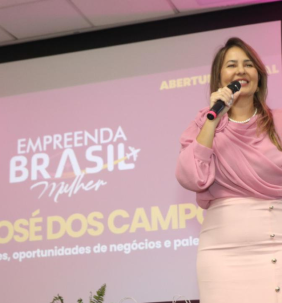 Fernanda Torres com blusa rosa segura microfone e gesticula durante abertura oficial do Empreenda Brasil Mulher em São José dos Campos, com projeção do evento ao fundo