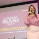 Fernanda Torres com blusa rosa segura microfone e gesticula durante abertura oficial do Empreenda Brasil Mulher em São José dos Campos, com projeção do evento ao fundo