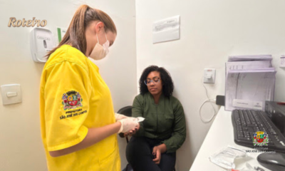 Profissional de saúde com uniforme amarelo e máscara da Prefeitura de São José dos Campos realiza atendimento a paciente sentada em consultório do Hospital de Clínicas Sul