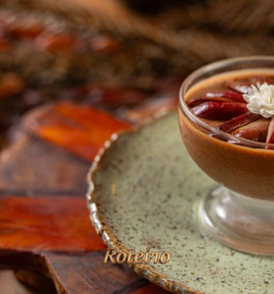 Taça de mousse de chocolate com pinhão do Festival do Donna Pinha, decorada com pinhões dispostos em leque e flor branca, servida em prato rústico verde com cascas de pinhão ao fundo. Foto: Douglas Fagundes