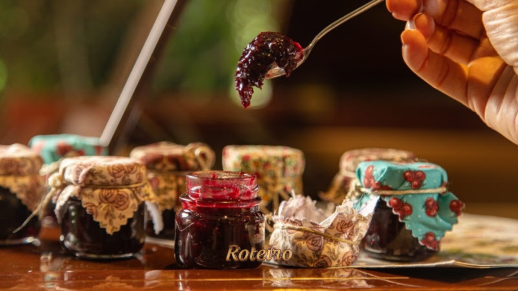 Mão segurando colher com geleia artesanal escura e brilhante sobre potes decorados com tecido floral, um dos mimos oferecidos às mães no restaurante Donna Pinha em Santo Antônio do Pinhal. Foto: Douglas Fagundes