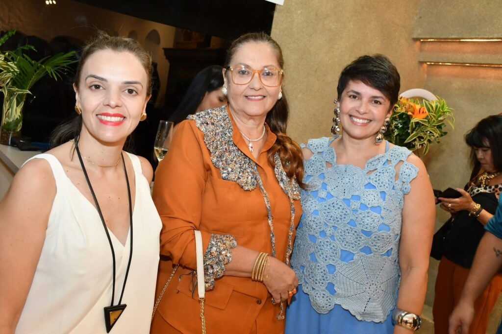 Três convidadas elegantemente vestidas posam no interior da Gregga Store durante o evento de aniversário de um ano da loja em São José dos Campos.