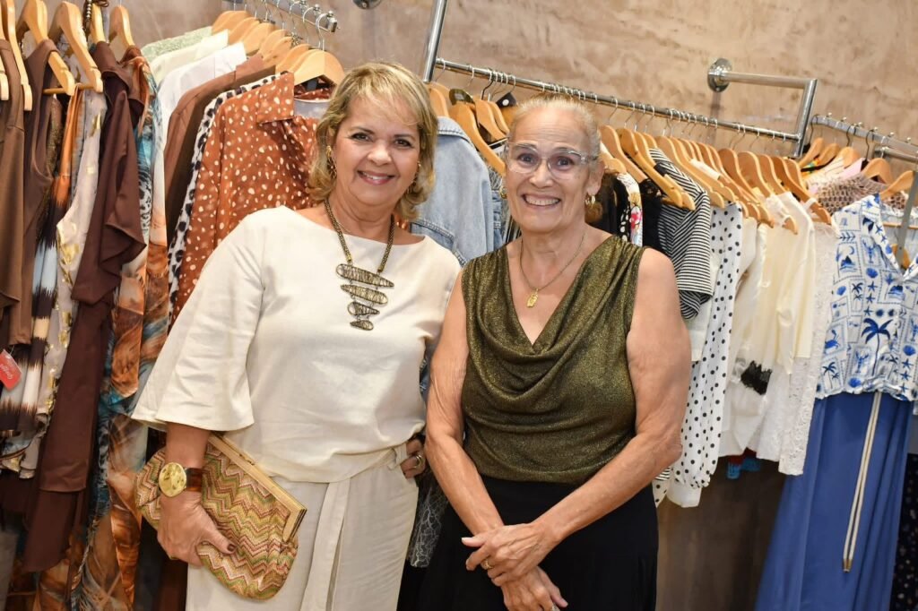 Duas clientes sorridentes posam em frente ao arara de roupas da Gregga Store durante o evento de aniversário de um ano da loja em SJC.