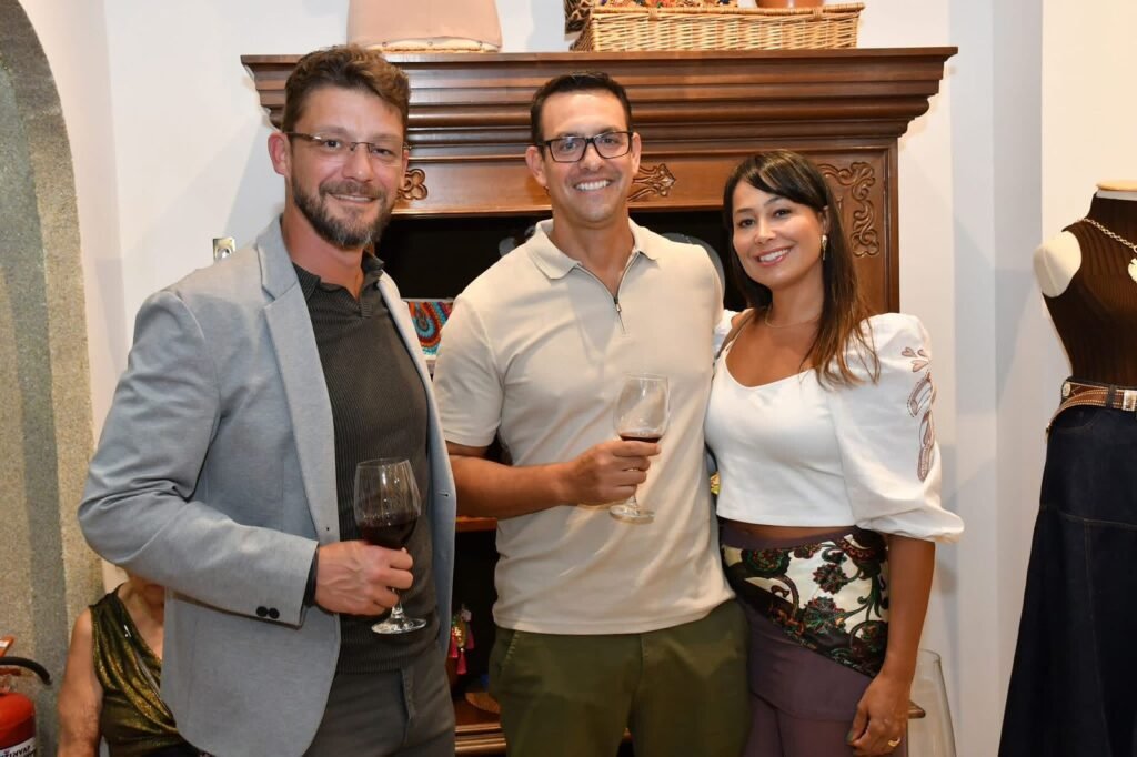 Trio de convidados — dois homens e uma mulher — posam sorrindo com taças de vinho durante o coquetel do aniversário da Gregga Store em SJC. Foto: Divulgação