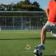 Jogador veterano com camiseta regata vermelha e short branco posa com o pé sobre uma bola de futebol em campo gramado de São José dos Campos, com trave ao fundo, em imagem de divulgação do Campeonato Joseense 50+ e 60+ da Prefeitura de SJC. Foto: PMSJC