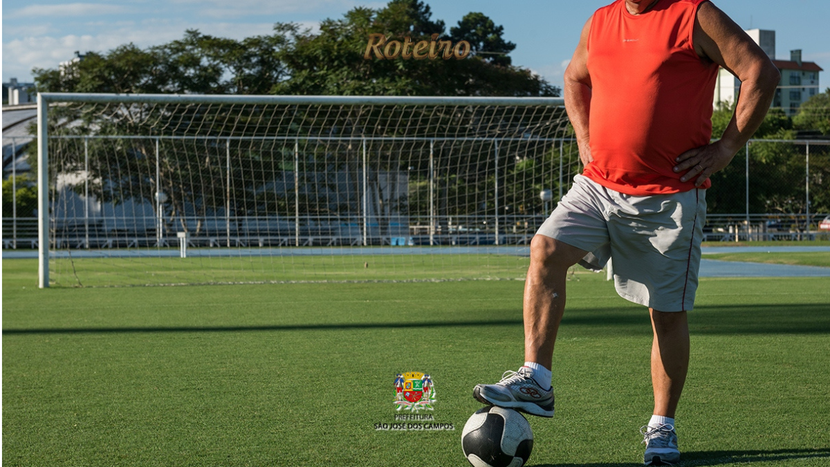 Jogador veterano com camiseta regata vermelha e short branco posa com o pé sobre uma bola de futebol em campo gramado de São José dos Campos, com trave ao fundo, em imagem de divulgação do Campeonato Joseense 50+ e 60+ da Prefeitura de SJC. Foto: PMSJC