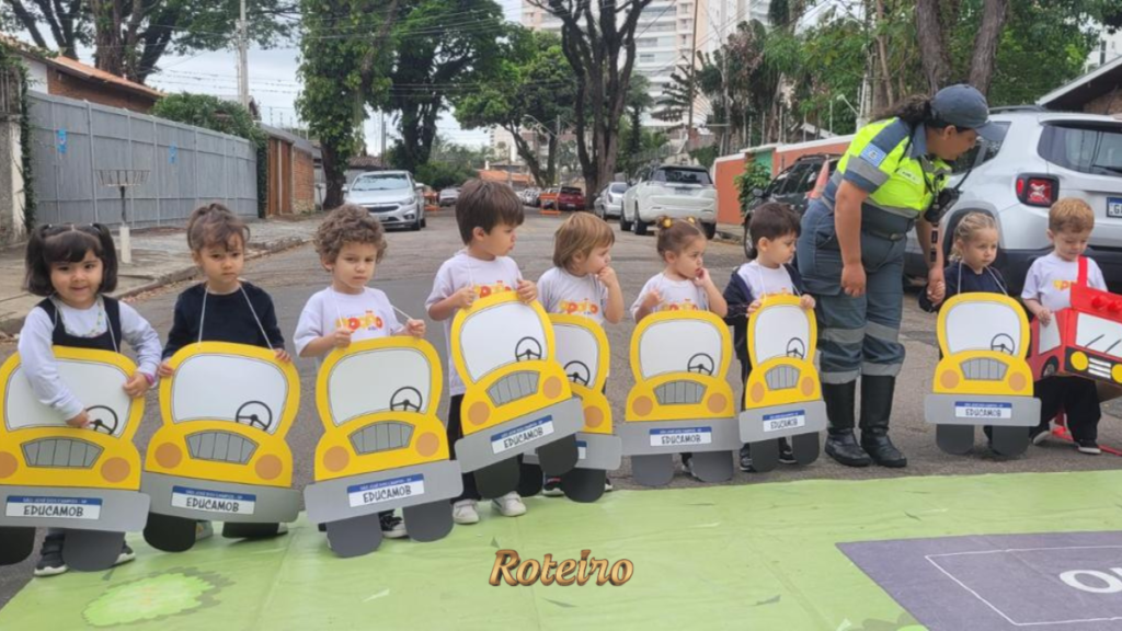 Crianças pequenas enfileiradas na rua segurando maquetes de carrinhos amarelos do programa Educamob, com agente de trânsito de colete verde ao lado, durante ação do Maio Amarelo em São José dos Campos. Foto: Divulgação/Shopping Jardim Oriente