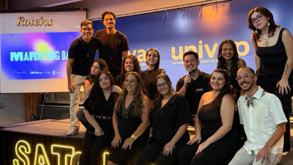Grupo de cerca de 12 estudantes e organizadores do Marketing Day 2026 posam no palco da UNIVAP em frente ao letreiro luminoso "SATORI" e ao banner do evento. Ao fundo, telão exibe o título "Marketing Day".