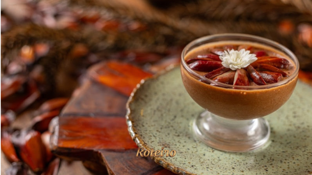 Taça de mousse de chocolate com pinhão do Festival do Donna Pinha, decorada com pinhões dispostos em leque e flor branca, servida em prato rústico verde com cascas de pinhão ao fundo. Foto: Douglas Fagundes