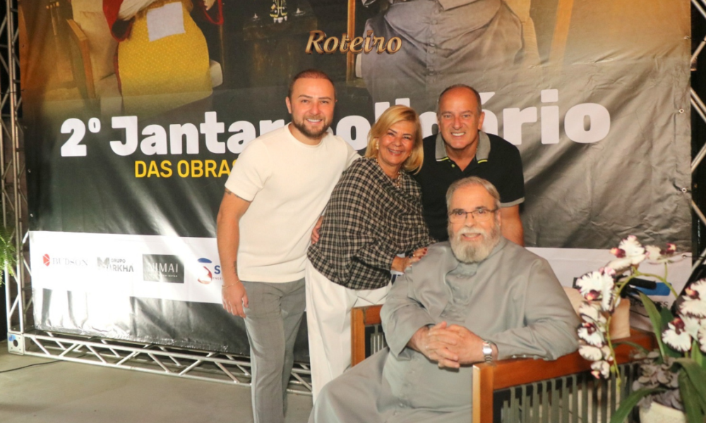 Padre Antônio Maria sentado ao centro com organizadores do evento em frente ao banner do 2º Jantar Solidário das Obras do Novo Caminho na Fazenda da Vovó, São José dos Campos. Foto: @nandojrfotografo