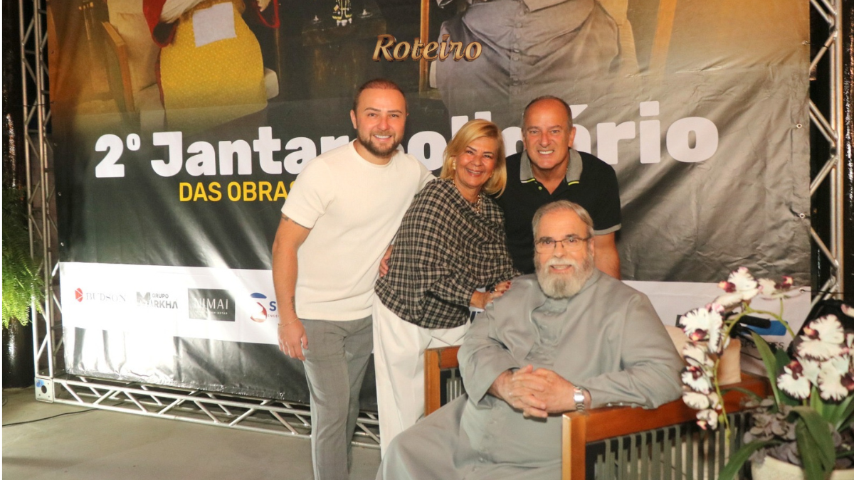 Padre Antônio Maria sentado ao centro com organizadores do evento em frente ao banner do 2º Jantar Solidário das Obras do Novo Caminho na Fazenda da Vovó, São José dos Campos. Foto: @nandojrfotografo