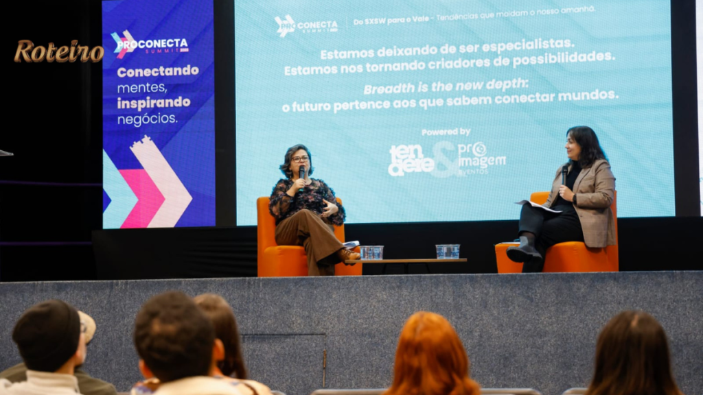 Duas mulheres sentadas em poltronas laranja no palco do ProConecta Summit durante talk sobre tendências do SXSW para o Vale do Paraíba. Telão ao fundo exibe a frase "Breadth is the new depth: o futuro pertence aos que sabem conectar mundos." Plateia vista de costas acompanha o debate.