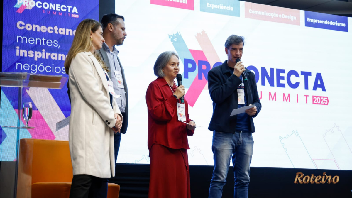 Quatro pessoas em pé no palco do ProConecta Summit 2025, no PIT São José dos Campos. Ao fundo, telão exibe o logo do evento e as trilhas: Audiovisual, Experiência, Comunicação e Design, e Empreendedorismo. Uma mulher de vestido vermelho e um homem de jaqueta preta seguram microfones durante apresentação.