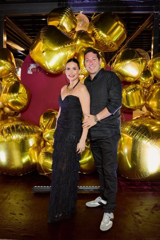 Casal sorri em frente a painel decorativo com balões dourados durante a comemoração dos cinco anos do Pátio Villa Branca em Jacareí, com logo do empreendimento ao fundo