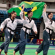 Três atletas da equipe Liga Vale de São José dos Campos com faixa preta celebram vitória segurando a bandeira do Brasil na Arena Carioca, no Rio de Janeiro, durante o Pan-Americano de Taekwondo 2026