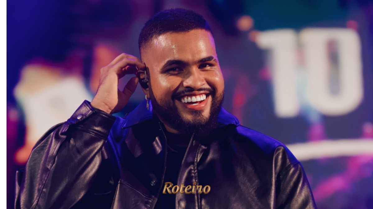Cantor Yan sorridente no palco, vestindo jaqueta de couro preta e segurando microfone, com iluminação roxa e cenário colorido ao fundo durante show. Foto: Divulgação