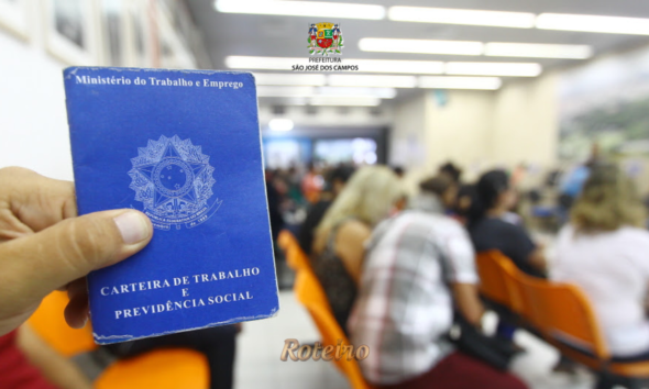 Pessoa segurando Carteira de Trabalho e Previdência Social em sala de espera do PAT de São José dos Campos com candidatos ao fundo