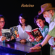 Integrantes do YULLE reunidos ao redor de piano de cauda folheando livros sobre Antonio Carlos Jobim e Elis Regina, em cena de divulgação do espetáculo tributo a Tom Jobim no Teatro Municipal de São José dos Campos. Foto: Divulgação