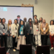Grupo de cerca de 18 participantes do congresso internacional posa para foto em sala da Saïd Business School da University of Oxford. Ao fundo, projetor exibe os logos da universidade. Logo do Portal RoteiroSJC no topo da imagem.