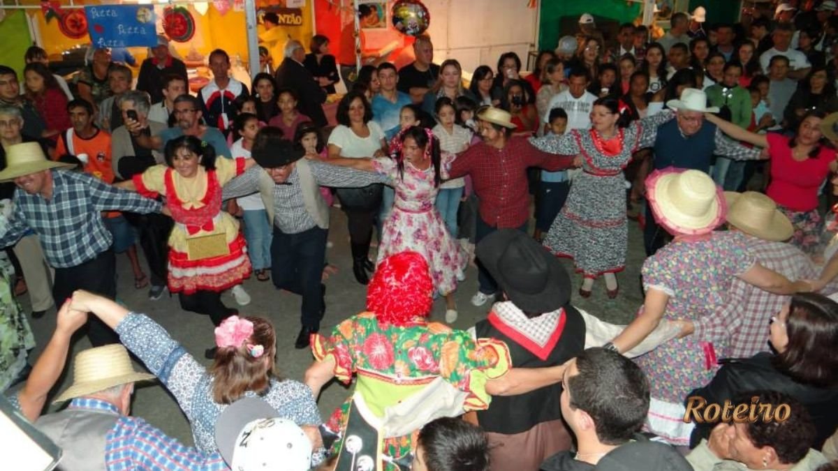 Festas Juninas SJC 2026. Pátio lotado, pessoas a carater dançando