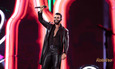 Cantor sertanejo no palco com microfone erguido e iluminação neon no Pinda Rodeio Fest 2026 — foto divulgação